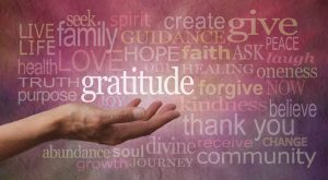 Multiple positive words, with a human hand holding the word gratitude on a purple background